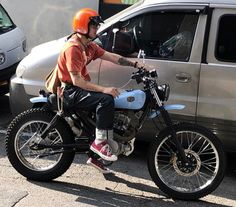 a man riding on the back of a dirt bike next to a silver van in a parking lot