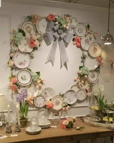 a table topped with lots of plates and vases filled with flowers next to a wall