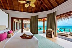 a bedroom with a large bed sitting under a ceiling fan next to an ocean view