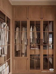 an organized closet with glass doors and wooden shelves filled with white clothing hanging on hangers