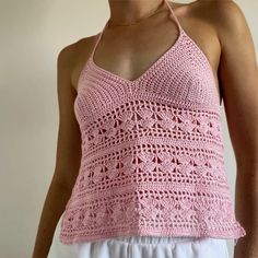 a woman wearing a pink crocheted tank top and white shorts with her hands in her pockets