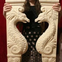 a woman holding up a large white sculpture with two dragon heads on it's sides