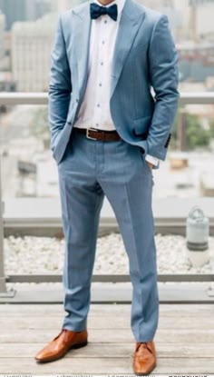 a man wearing a blue suit and bow tie standing on a balcony with his hands in his pockets