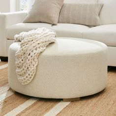 a living room with a white couch and round ottoman on the floor next to a window