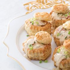 some biscuits are sitting on a white plate with green onions and mayonnaise drizzled over them