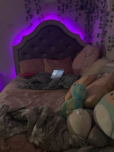 a bed with stuffed animals on it and a laptop computer sitting on the headboard