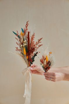 two hands holding flowers tied to each other on a beige background with white ribbon around them