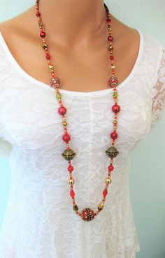 Red beaded woman's necklace handmade by Ralston Originals. Click to see this stunning red necklace with a variety of beads. This beautiful necklace is perfect to for a formal occasion, or for everyday. Red jewelry is perfect for the holidays too. This necklace is made with an assortment of beads. The focal bead at the bottom is a large red colored bead with detailed gold metal accents, and crystal rhinestones. There are two more similar beads in the necklace. The other beads include, crystal bea Red Beaded Long Necklace As Gift, Red Beaded Long Necklace For Gift, Elegant Handmade Red Long Necklace, Bohemian Long Red Necklace, Red Beaded Long Necklace, Red Bohemian Beaded Necklaces With Large Beads, Red Bohemian Necklace With Round Beads, Bohemian Red Beaded Necklaces With Large Beads, Red Jewelry With Gold Beads For Jewelry Making