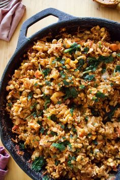 a skillet filled with rice and vegetables on top of a wooden table next to bread