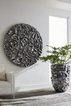 a living room with a large metal sculpture on the wall next to a chair and potted plant