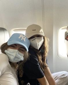 two people wearing face masks while sitting on an airplane seat with their arms around each other