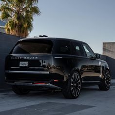 the black range rover is parked in front of a building with palm trees behind it