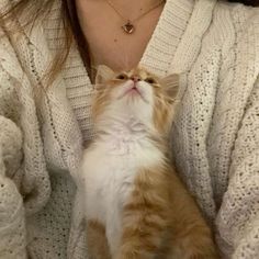 a woman is holding a cat in her lap while wearing a white sweater and gold necklace