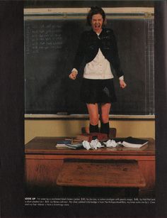 a woman standing on top of a desk in front of a blackboard