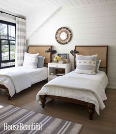 two twin beds in a bedroom with white walls and wood flooring, along with a rug on the floor