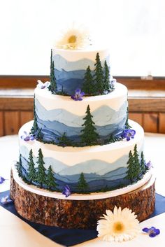 a three tiered cake with pine trees and flowers on the top is sitting on a table