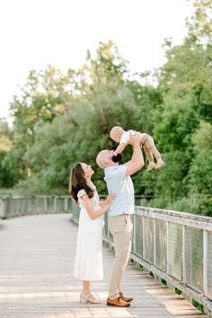 a man holding a baby up in the air while standing next to a woman on a bridge