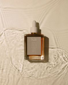 a bottle of sea cologne sitting on top of a white surface with water swirling around it