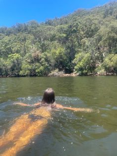 a woman swimming in the water with trees behind her on a sunny day at the lake