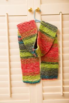 a pair of colorful knitted mitts hanging from a hook on a white door