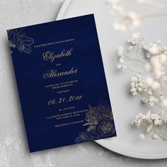 a blue and gold wedding card on a plate next to some white baby's breath flowers