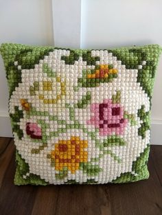 a pillow made out of plastic beads with flowers on the front and sides, sitting on top of a wooden floor