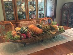 a wooden tray filled with lots of vegetables on top of a table next to a china cabinet