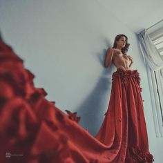 a woman in a long red dress standing next to a window and looking at herself in the mirror