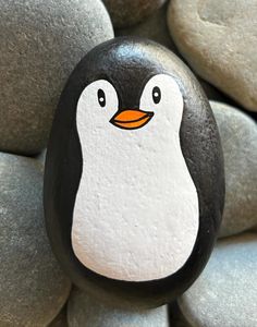 a rock with a penguin painted on it sitting in front of some rocks and pebbles