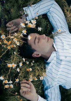 a man laying in the grass with daisies on his head and eyes closed,