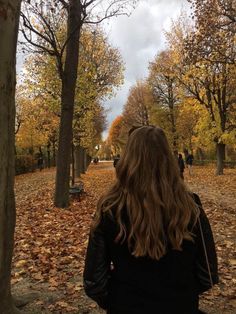 a woman is walking through an autumn park