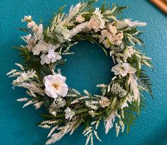 a wreath with white flowers and greenery on a blue wall