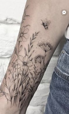 a woman's arm with flowers and a bee tattoo on the back of her arm