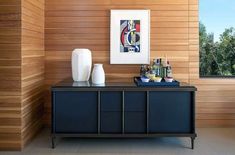 a black cabinet with two white vases on top of it next to a wooden wall