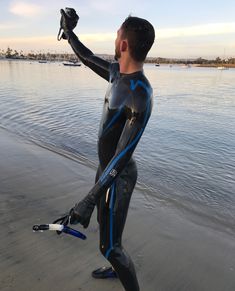 a man in a full body wetsuit standing on the beach with his hands up