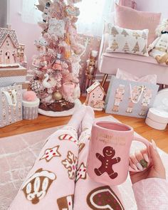 a person holding a pink coffee mug in front of a christmas tree with gingerbreads on it