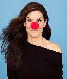 a woman wearing a red nose and black top with her hair blowing in the wind