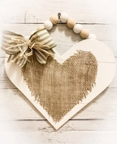 a heart shaped wooden sign with a bow on it's side and some wood beads around the edge