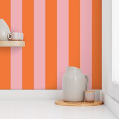 an orange and pink striped wallpaper in a kitchen with white countertop, utensils and cups