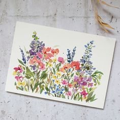 a watercolor painting of colorful flowers on a white paper next to some dried grass