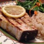 a plate topped with meat and rice next to a lemon wedge on top of a table