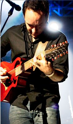 a man playing an acoustic guitar while standing in front of a microphone and stage lights