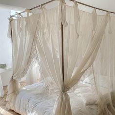 a canopy bed with white sheets and drapes on the top, in a bedroom