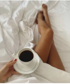 a woman is laying in bed with her legs crossed and holding a cup of coffee