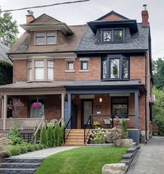 a brick house with many windows and steps leading up to the front door on a residential street