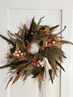 a wreath hanging on the front door with orange and white flowers, leaves and berries