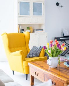 a living room with yellow chairs and flowers in a vase on the coffee table next to it