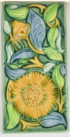 a ceramic tile with yellow flowers and leaves on the bottom, surrounded by green foliage