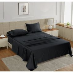 a bed with black sheets and pillows in a room next to a lamp on a table