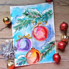 a watercolor christmas card with ornaments on the table next to it and a snowflake